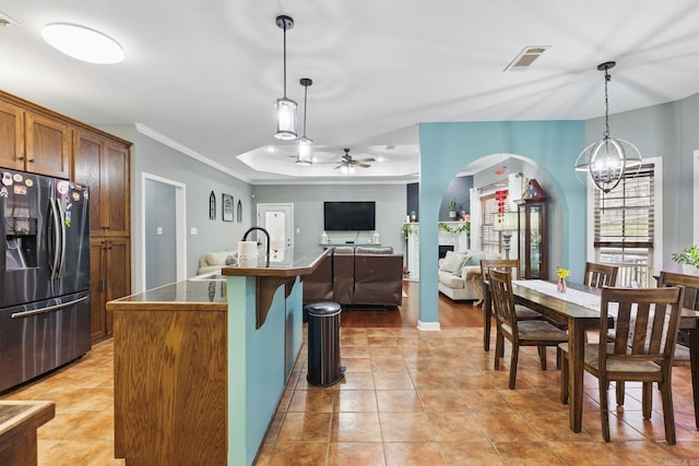 kitchen with a tray ceiling, pendant lighting, stainless steel refrigerator with ice dispenser, visible vents, and a sink