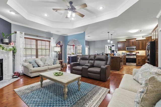 living room featuring visible vents, a raised ceiling, a fireplace with flush hearth, ornamental molding, and wood finished floors