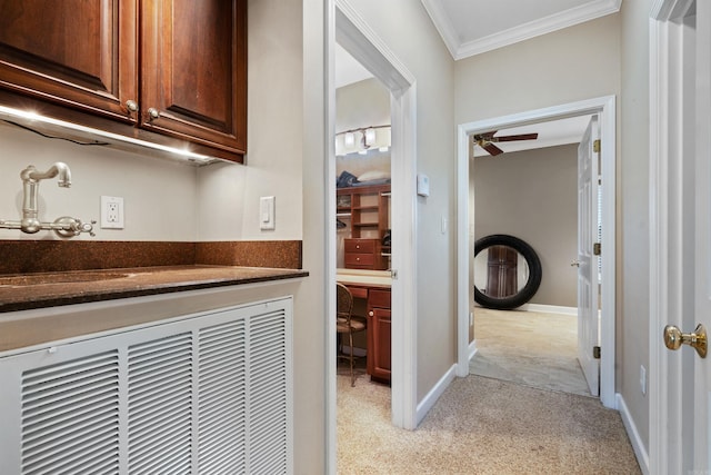 corridor featuring a sink, light colored carpet, baseboards, and ornamental molding