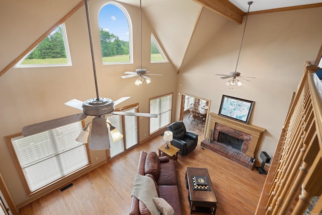 living area with visible vents, ceiling fan, beam ceiling, a fireplace, and wood finished floors