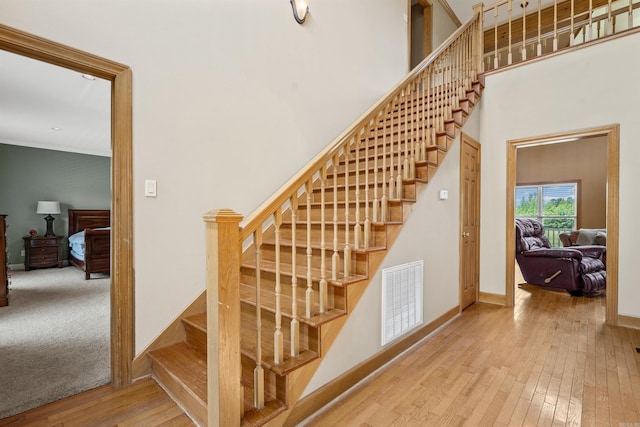 staircase featuring visible vents, wood-type flooring, baseboards, and a towering ceiling