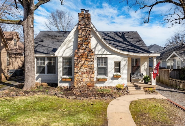 tudor-style house featuring brick siding, covered porch, a chimney, and fence