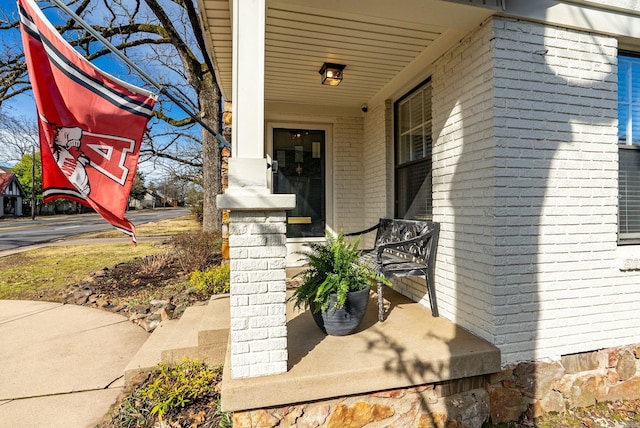 view of exterior entry featuring brick siding and a porch