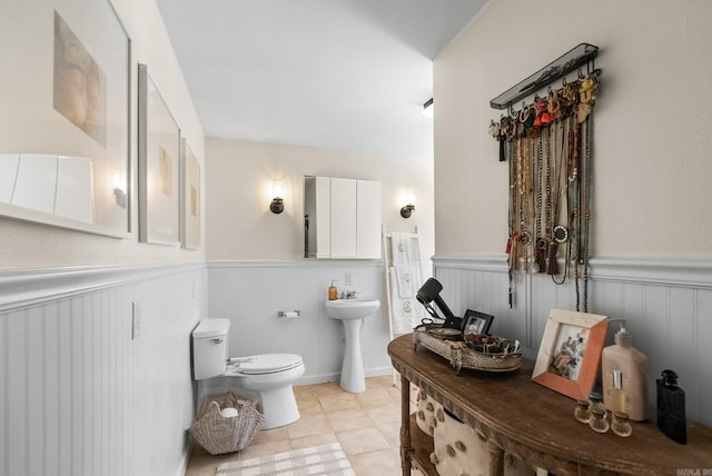 bathroom with tile patterned flooring, a wainscoted wall, toilet, and a sink