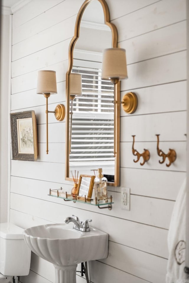 half bath with wooden walls, ornamental molding, and a sink