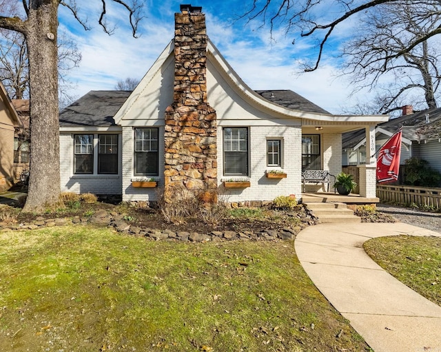 view of front of property with a front lawn, brick siding, a porch, and a chimney