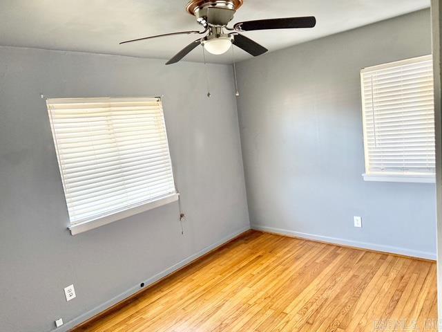 empty room featuring ceiling fan, baseboards, and wood finished floors