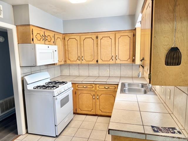 kitchen with visible vents, tile countertops, decorative backsplash, white appliances, and a sink