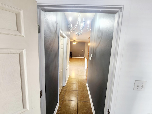 corridor with tile patterned floors, baseboards, and a chandelier