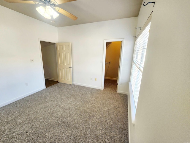 unfurnished bedroom featuring a spacious closet, carpet flooring, a ceiling fan, and baseboards