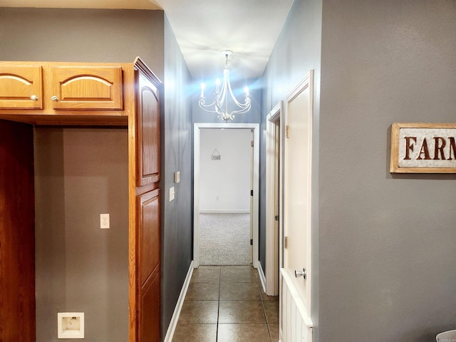 hallway with dark tile patterned flooring, a notable chandelier, and baseboards