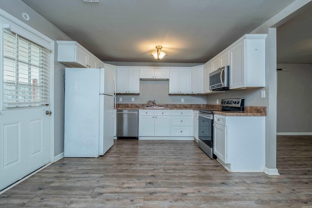 kitchen with light wood finished floors, baseboards, white cabinets, stainless steel appliances, and a sink