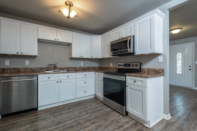 kitchen with a sink, appliances with stainless steel finishes, wood finished floors, and white cabinetry