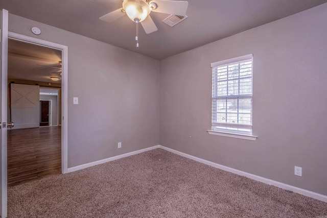 unfurnished room featuring visible vents, a barn door, a ceiling fan, and carpet flooring