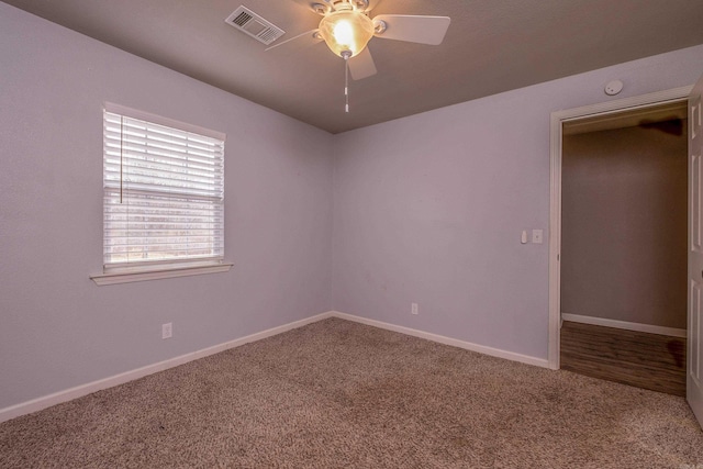 carpeted spare room with visible vents, baseboards, and ceiling fan