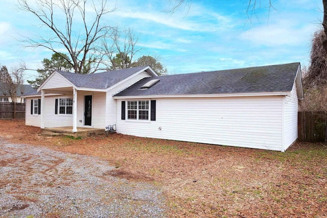 ranch-style house featuring a porch, roof with shingles, and fence