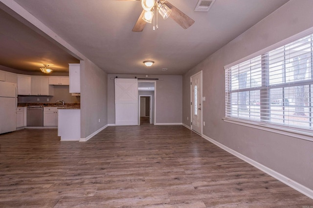 unfurnished living room with visible vents, a sink, dark wood-style floors, a barn door, and ceiling fan