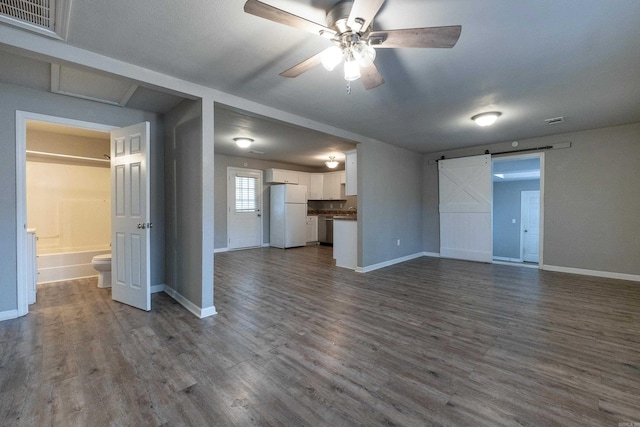 unfurnished living room with a barn door, baseboards, visible vents, and dark wood finished floors