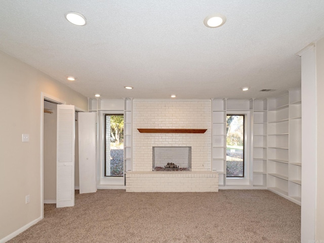 unfurnished living room with a brick fireplace, carpet, and a wealth of natural light