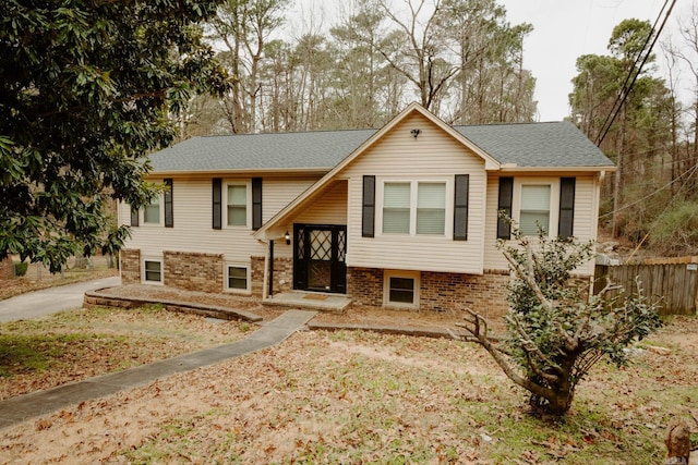 raised ranch featuring fence, brick siding, and roof with shingles