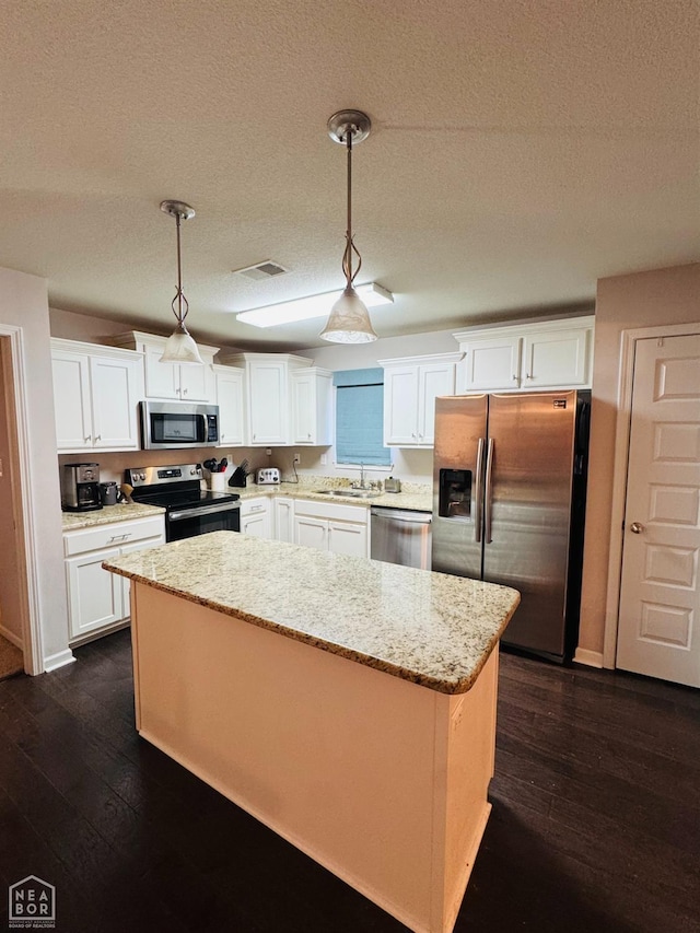 kitchen featuring a kitchen island, light stone counters, white cabinets, stainless steel appliances, and a sink