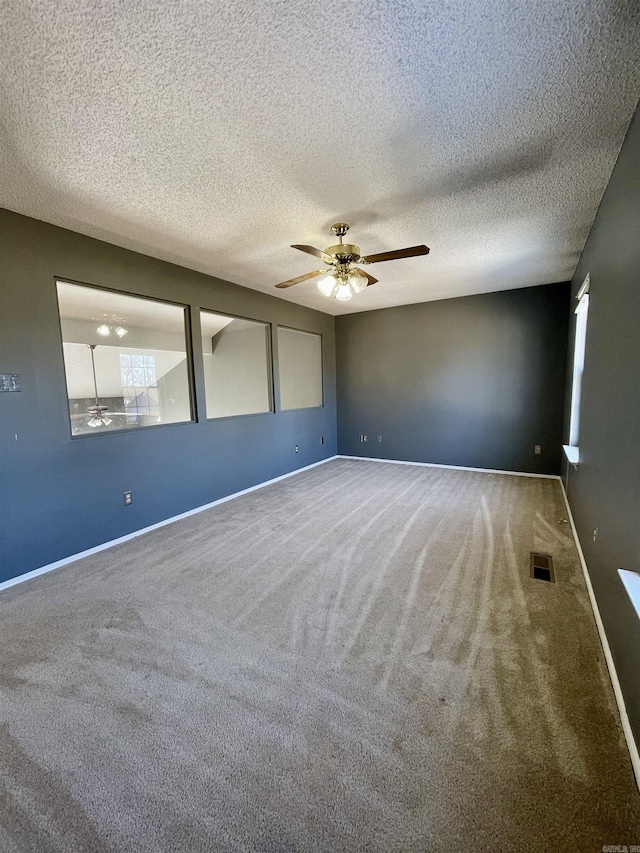 carpeted spare room featuring visible vents, a textured ceiling, baseboards, and a ceiling fan