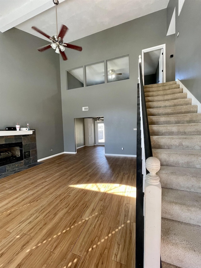 unfurnished living room featuring stairway, wood finished floors, a glass covered fireplace, high vaulted ceiling, and a ceiling fan