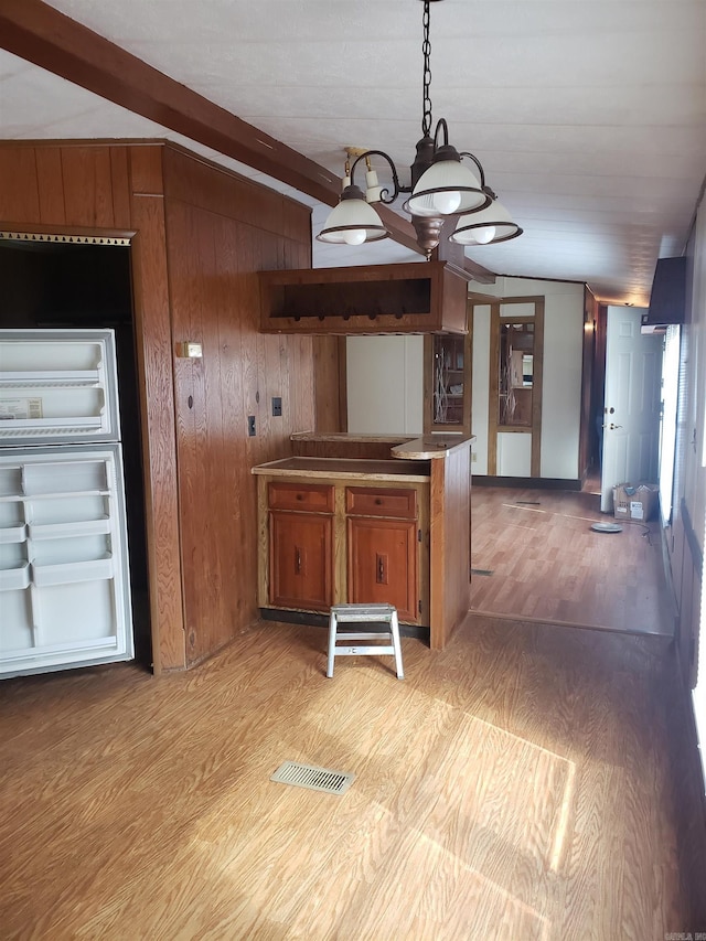 kitchen with beamed ceiling, brown cabinets, pendant lighting, light wood-style flooring, and wooden walls