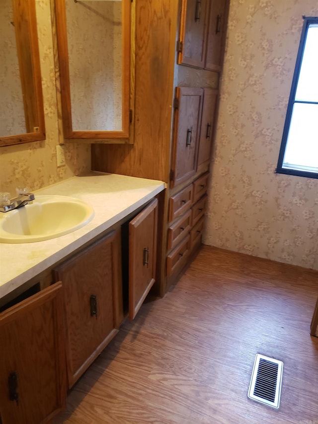 bathroom with wallpapered walls, wood finished floors, vanity, and visible vents