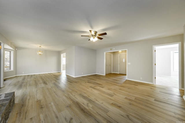 unfurnished living room featuring baseboards, light wood-style flooring, and ceiling fan with notable chandelier