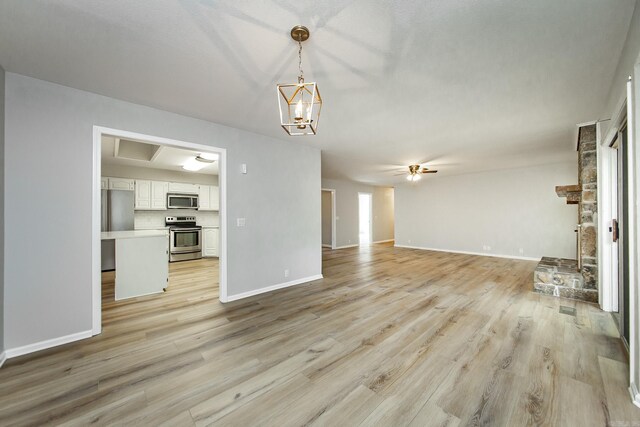 unfurnished living room with ceiling fan with notable chandelier, baseboards, and light wood-style floors