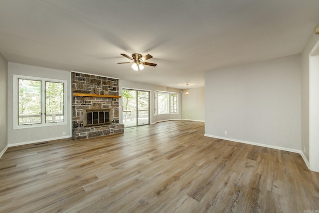 unfurnished living room with a stone fireplace, baseboards, and wood finished floors