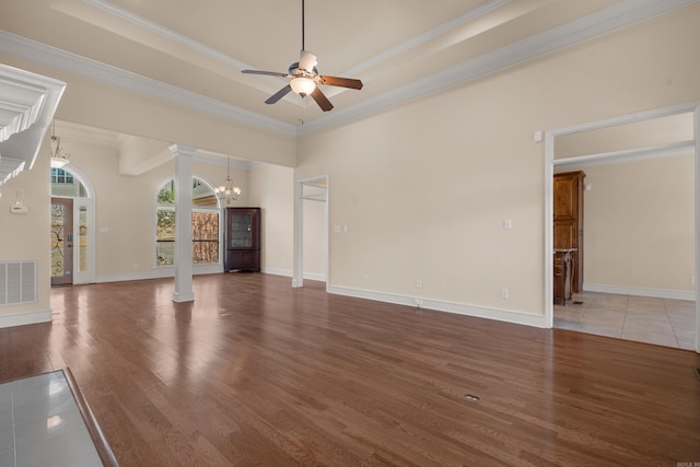 unfurnished living room with wood finished floors, visible vents, a tray ceiling, decorative columns, and ceiling fan with notable chandelier