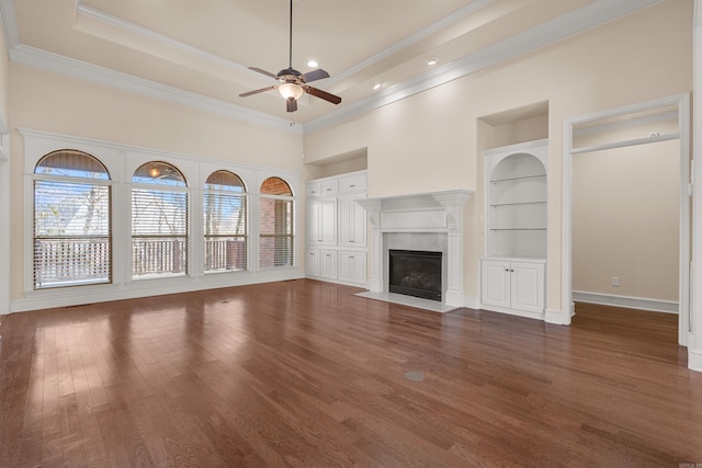 unfurnished living room featuring built in features, a fireplace, ceiling fan, ornamental molding, and dark wood-type flooring