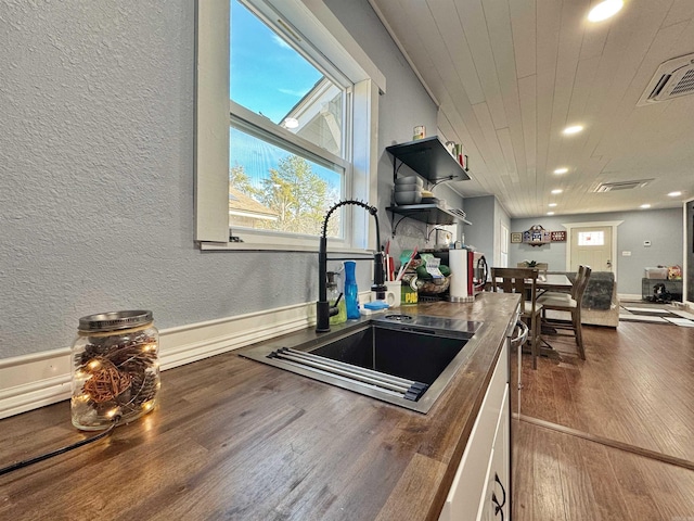 kitchen with wood finished floors, visible vents, a sink, wood ceiling, and a textured wall