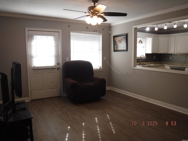 living area with wood finished floors, a ceiling fan, baseboards, and ornamental molding