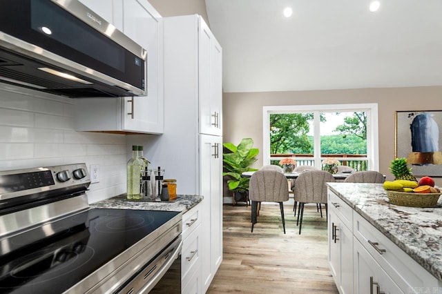 kitchen featuring tasteful backsplash, light stone countertops, light wood-style flooring, appliances with stainless steel finishes, and white cabinetry