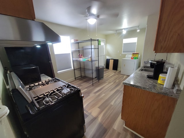 kitchen featuring dark countertops, range hood, light wood-style floors, brown cabinetry, and washer / clothes dryer