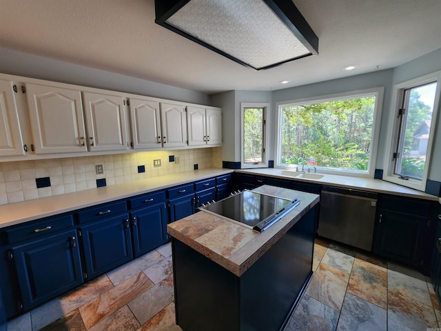 kitchen featuring blue cabinetry, a sink, backsplash, stainless steel dishwasher, and stone tile floors