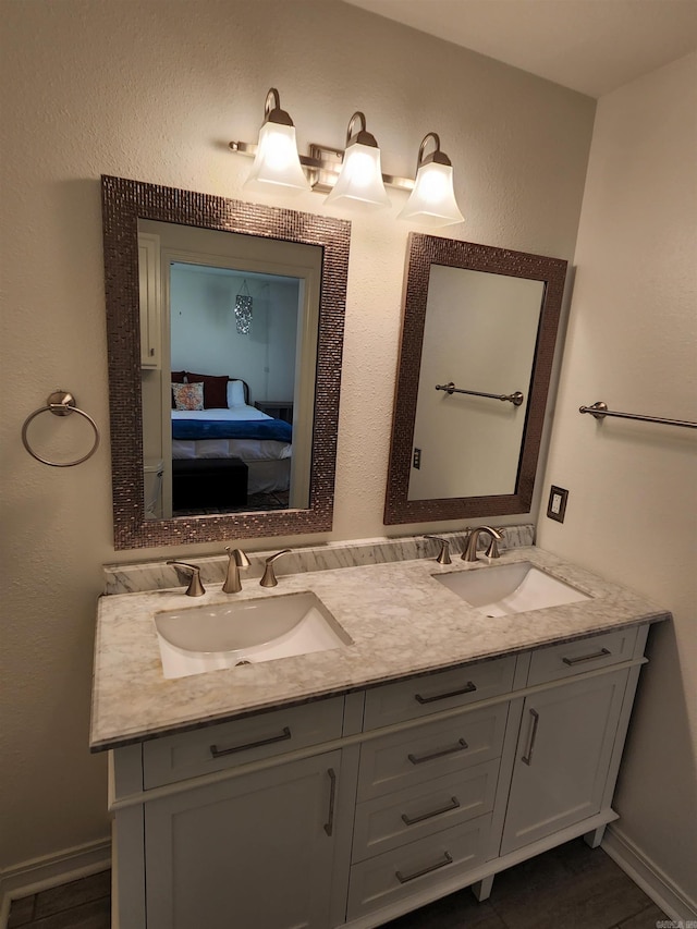 ensuite bathroom featuring double vanity, connected bathroom, baseboards, and a sink