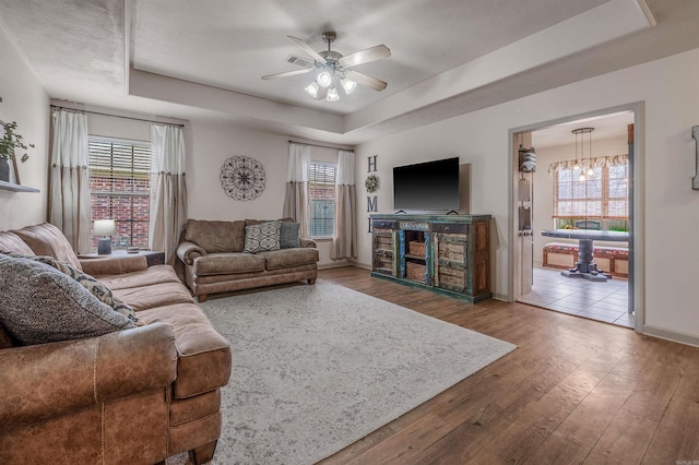 living room with a raised ceiling, hardwood / wood-style flooring, a ceiling fan, and baseboards