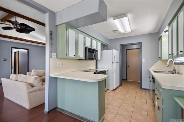 kitchen with green cabinetry, freestanding refrigerator, a sink, light countertops, and black microwave