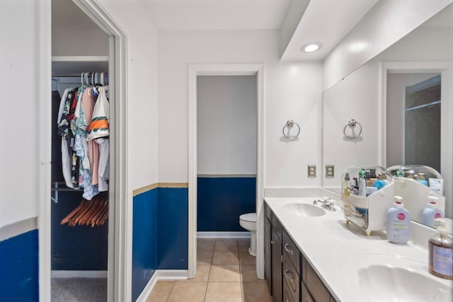 full bath featuring double vanity, a sink, tile patterned flooring, a walk in closet, and toilet