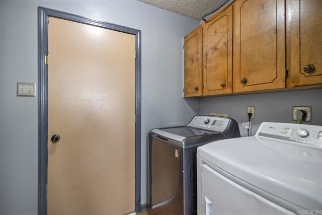 laundry room with cabinet space, a textured ceiling, and washer and clothes dryer