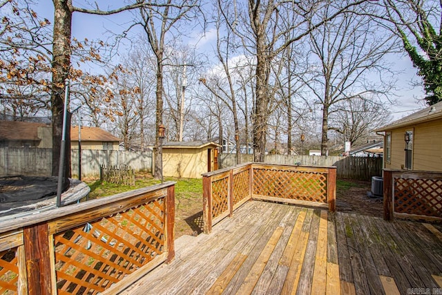 deck featuring an outbuilding, central AC unit, a shed, a fenced backyard, and a trampoline