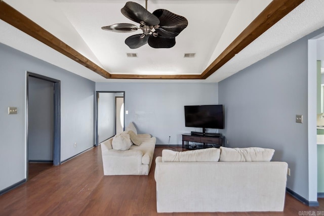 living room with a tray ceiling, visible vents, and dark wood-style floors