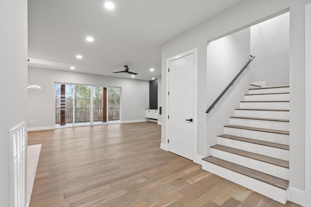 unfurnished living room with light wood-style flooring, recessed lighting, baseboards, ceiling fan, and stairs