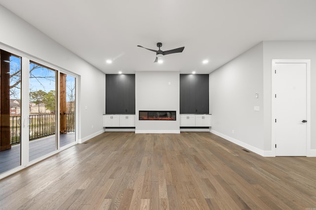 unfurnished living room with baseboards, recessed lighting, wood finished floors, a glass covered fireplace, and a ceiling fan