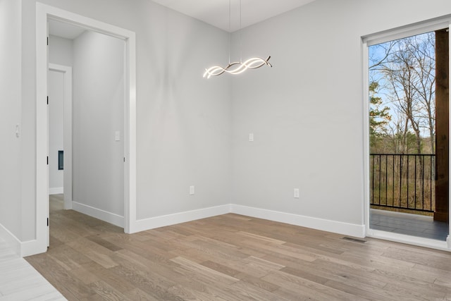 unfurnished dining area featuring light wood-style flooring, a notable chandelier, visible vents, and baseboards