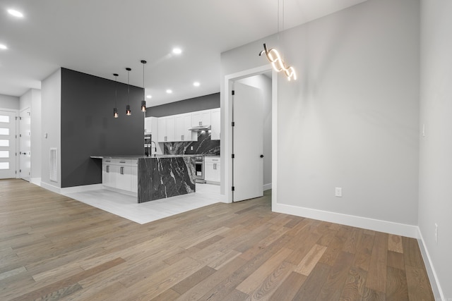 kitchen featuring light wood-style flooring, under cabinet range hood, backsplash, white cabinets, and hanging light fixtures